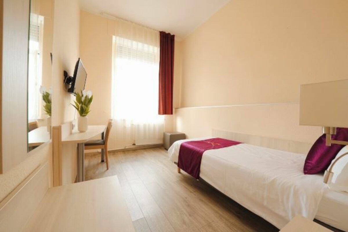 A hotel room with a bed, a desk, a chair, and a window with curtains.