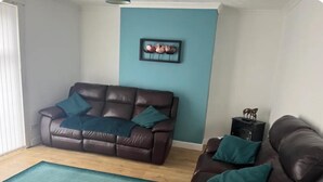 Ein Wohnzimmer mit einem braunen Ledersofa, türkisfarbenen Kissen, einem türkisfarbenen Teppich und einem gerahmten Bild an der Wand.