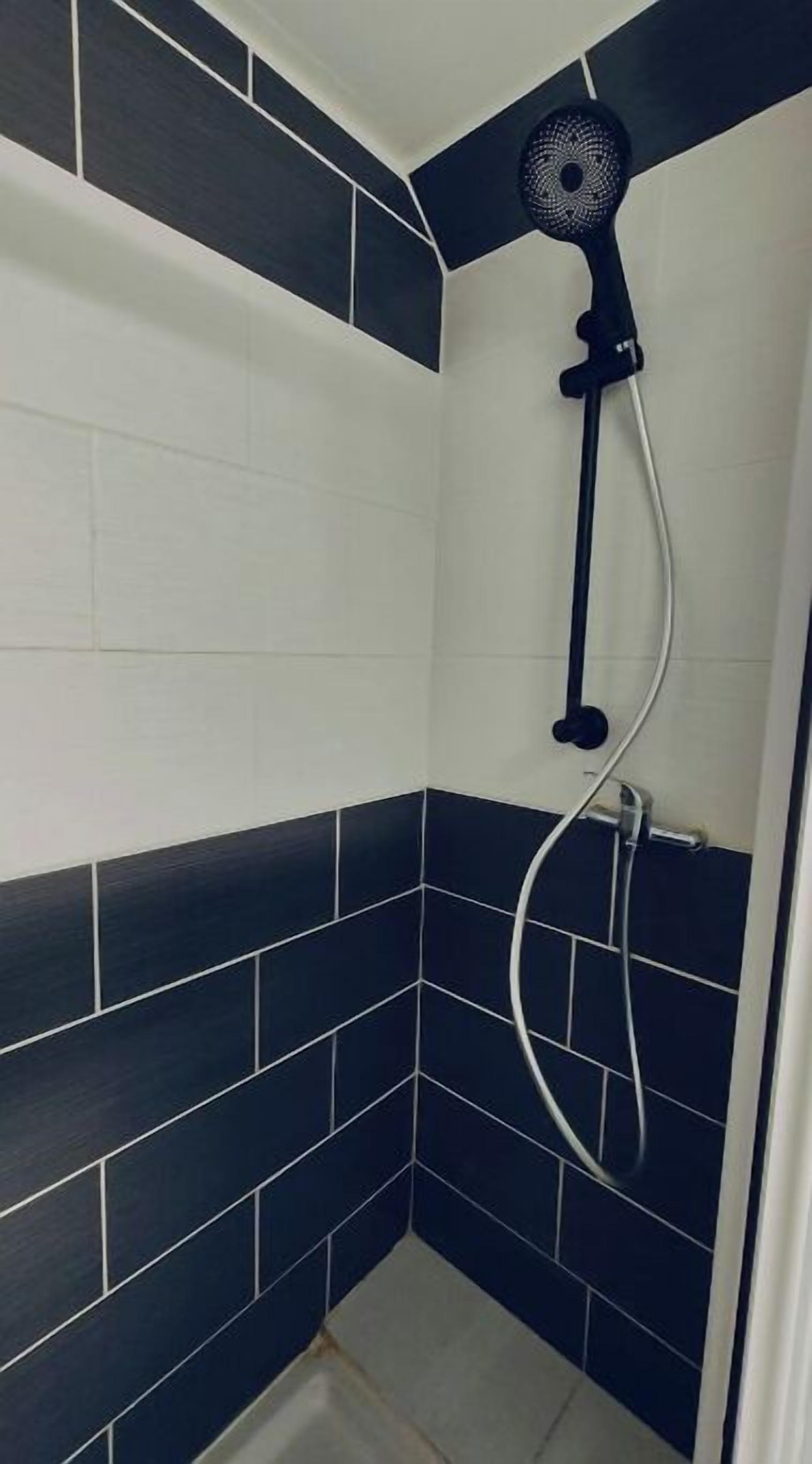A shower with a black and white tiled wall, a handheld showerhead, and a wall-mounted fan.