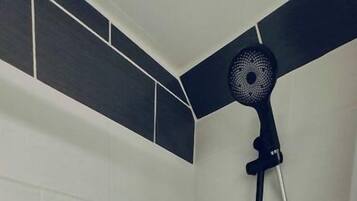 A shower with a black and white tiled wall, a handheld showerhead, and a wall-mounted fan.