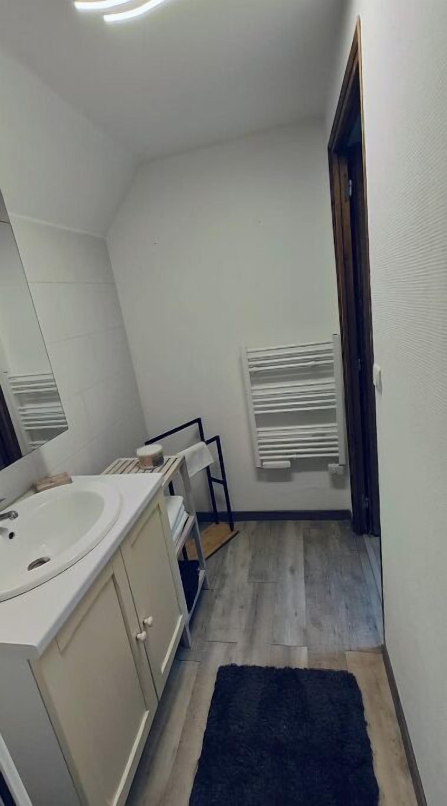A small, narrow bathroom with a white sink, mirror, and a towel rack.