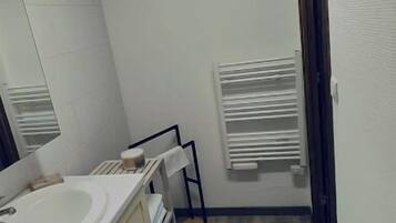 A small, narrow bathroom with a white sink, mirror, and a towel rack.