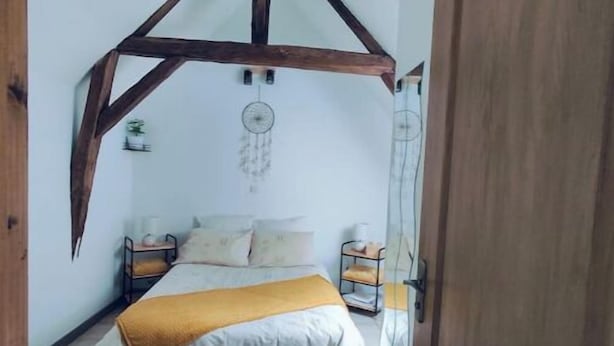 A bedroom with a sloped ceiling, a bed with a white comforter and a yellow throw, a nightstand, and a dreamcatcher.