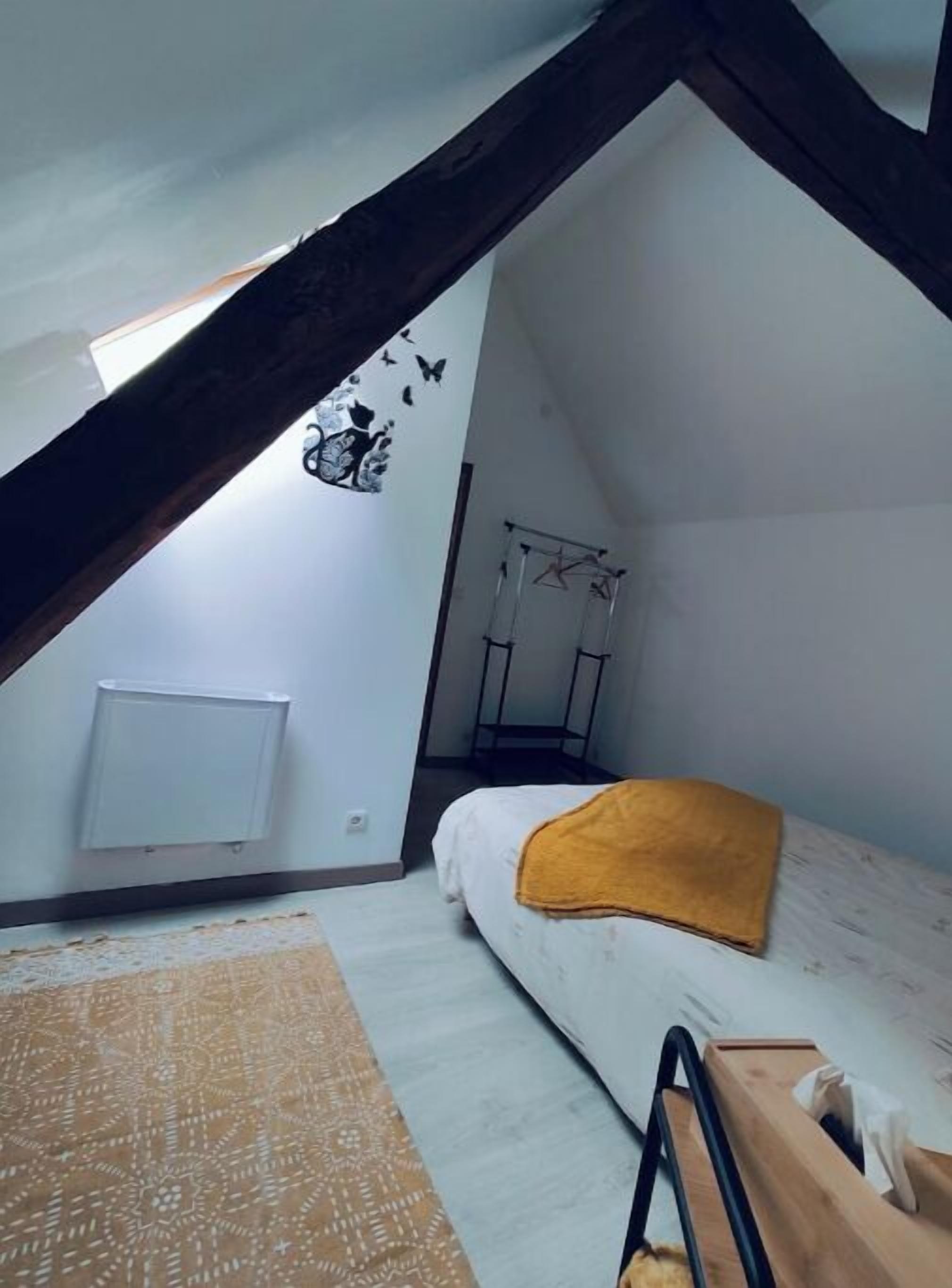 Ein kleines Schlafzimmer im Dachgeschoss mit schrägen Wänden, einem Bett mit gelber Decke, einem Heizkörper und einer Wandhalterung für Wäsche.