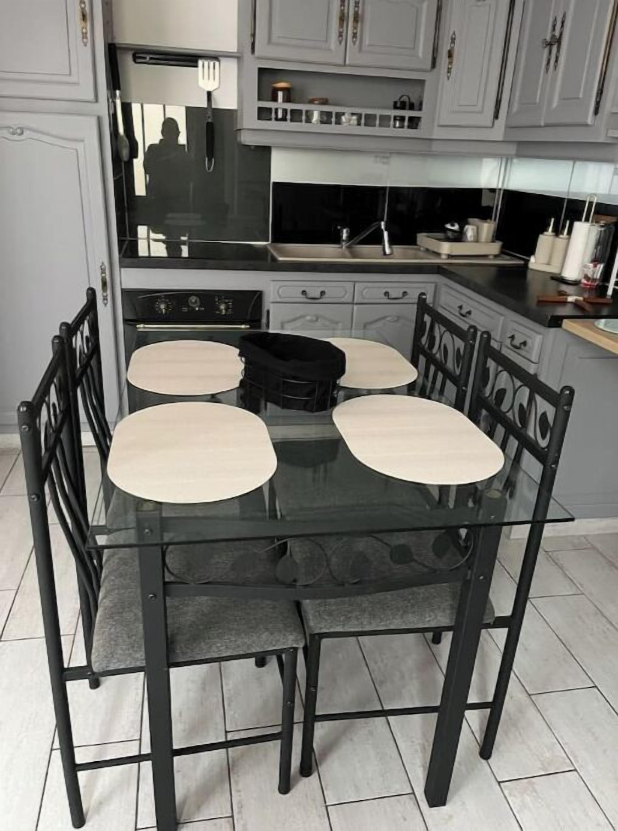 Zona pranzo con tavolo in vetro e quattro sedie, piano cottura e pensili in cucina.