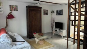 A living room with a sofa, a glass coffee table, a TV on a white stand, a wooden cabinet, and a staircase.
