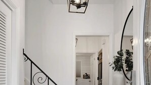 Ein Flur mit einem gemusterten Teppich, einer Treppe mit aufwendiger Geländer und einer Pendelleuchte, sowie einer Tür mit Spiegel und Pflanze.