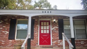 A brick building with a red door, two windows with shutters, and a small porch with steps. - Peaceful Home In The Heart of TLH (Tallahassee)