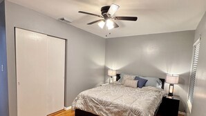 A bedroom with a bed, a ceiling fan, a nightstand with a lamp, and a door. - Peaceful Home In The Heart of TLH (Tallahassee)