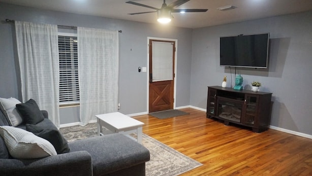 A living room with a gray sofa, white coffee table, wooden flooring, a TV, and a fireplace. - Peaceful Home In The Heart of TLH (Tallahassee)