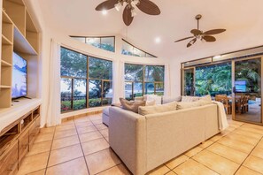A spacious living room with a large sofa, a television, and a ceiling fan.