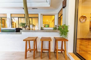 Un interior moderno con tres taburetes de madera, una planta en maceta y un ventanal con vistas.