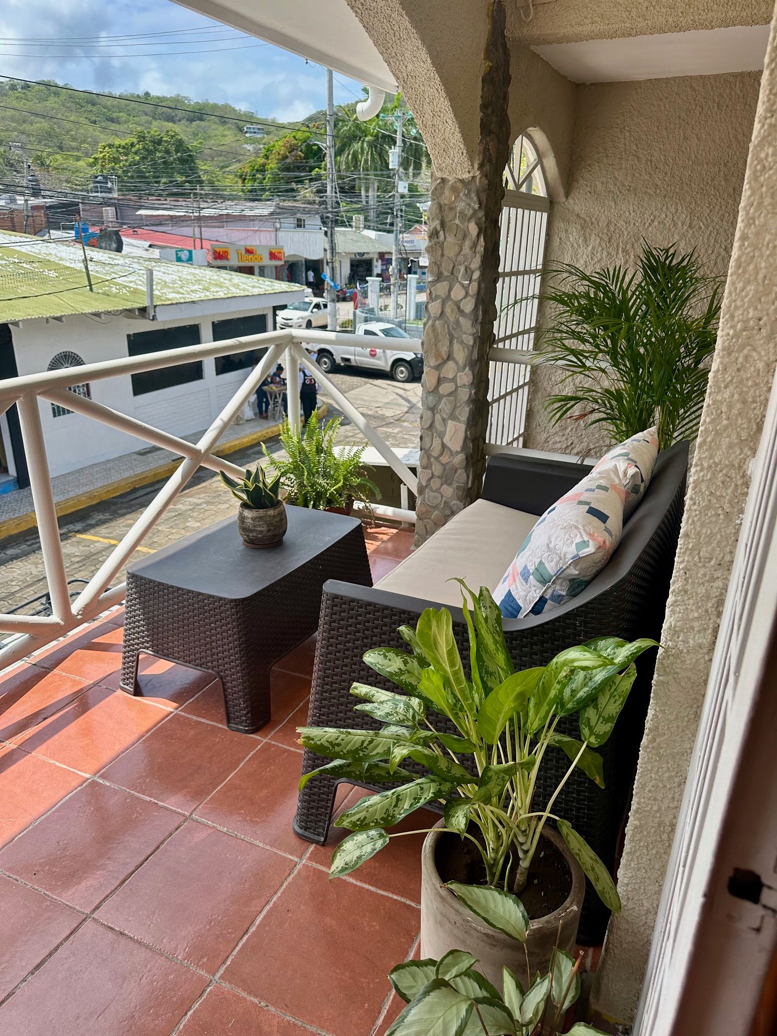 A balcony with wicker furniture, a potted plant, and a view of the street.
