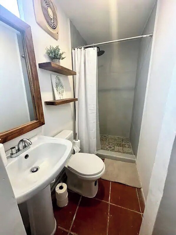 Une petite salle de bain avec un lavabo, des toilettes et une douche, le tout de couleur blanche.