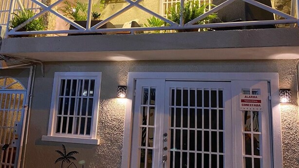 Een gebouw met twee verdiepingen met een balkon, een bord met 'DRIFTWOOD HOMES & RENTALS Nicaragu' en een beveiligingsalarmsysteem.