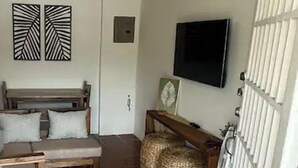 Een ruimtelijk ingerichte leefruimte met een bank, een klein tafeltje, een flatscreen televisie aan de wand en een betegelde vloer.