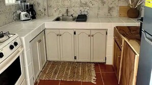 Een kleine keuken met witte kastjes, een inbouwfornuis, een spoelbak en een koelkast.