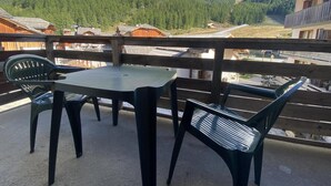 En balkong med ett bord och stolar, med utsikt över ett bergigt landskap med trähus.