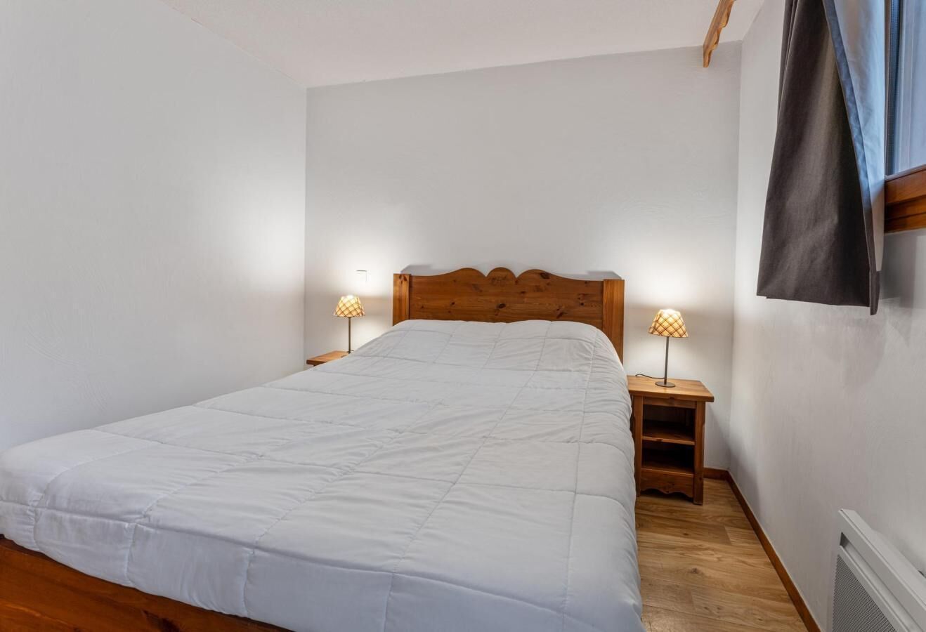 Une chambre à coucher avec un grand lit, une tête de lit en bois, deux tables de chevet avec des lampes et un radiateur.