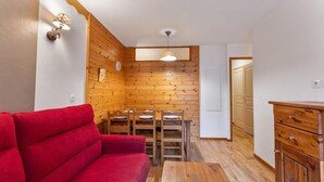 Ett litet rum med en väggpanel av trä, en röd soffa, ett matbord i trä med stolar och ett träskåp.
