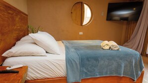 A hotel room with a wooden headboard, a bed with white linens, a blue blanket, and two rolled towels on the bed.