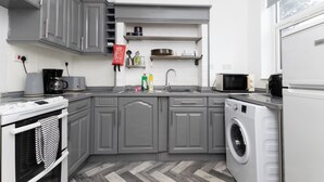 A modern kitchen with grey cabinets, a built-in oven, a microwave, a washing machine, and a sink.