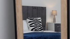 A neatly made bed with a dark blue bedspread and a pillow with a black leaf pattern.