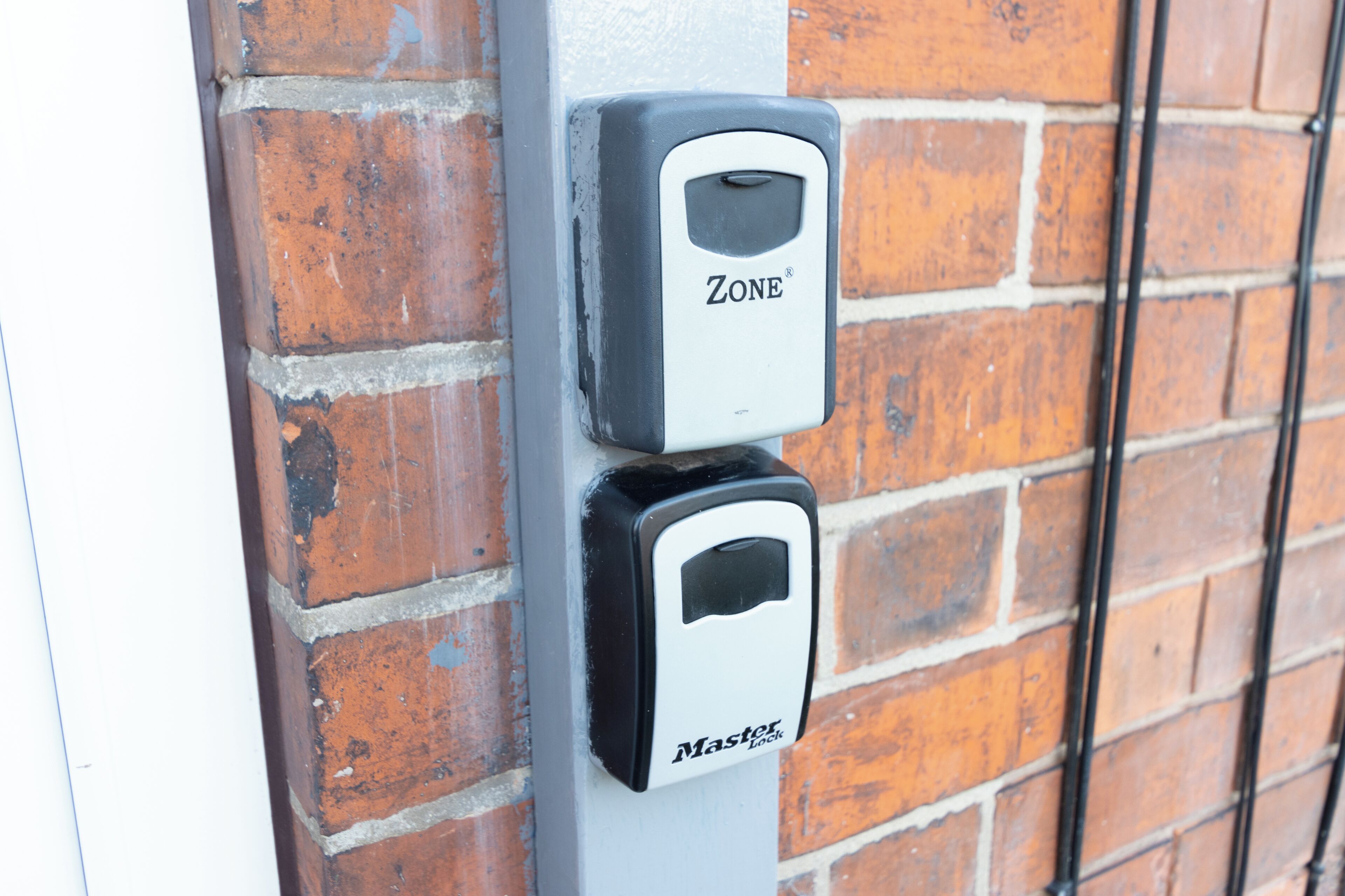 A security device labeled "ZONE" and "Master Lock" attached to a brick wall.