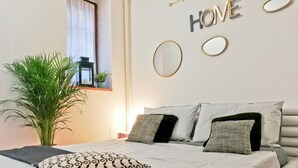 Ein ordentlich bezogenes Bett mit gemusterten Kissen, eine große Topfpflanze und eine Wand mit dekorativen Buchstaben und Spiegeln.