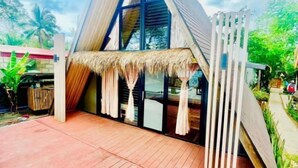 Un bâtiment moderne de forme triangulaire, doté d’une terrasse en bois et d’un toit de chaume.