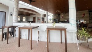 A modern interior with a central bar area, white chairs, and wooden tables. - Suite Room 1 (Sipalay City)