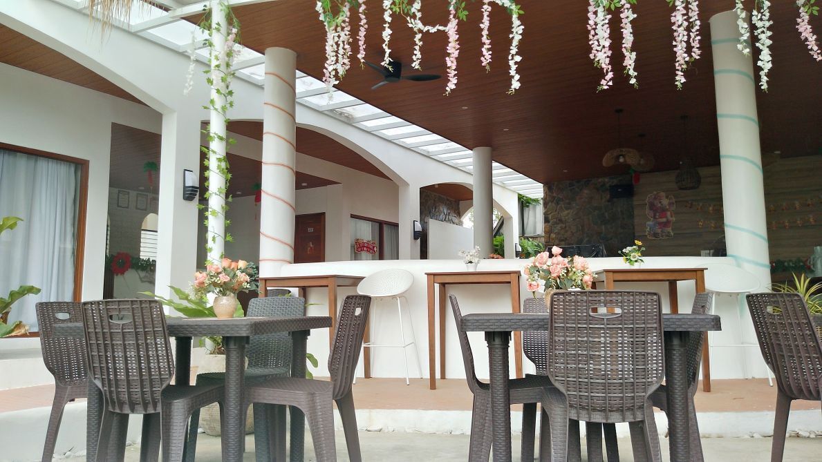 An outdoor seating area with wicker chairs and tables, a bar counter, and hanging floral decorations.