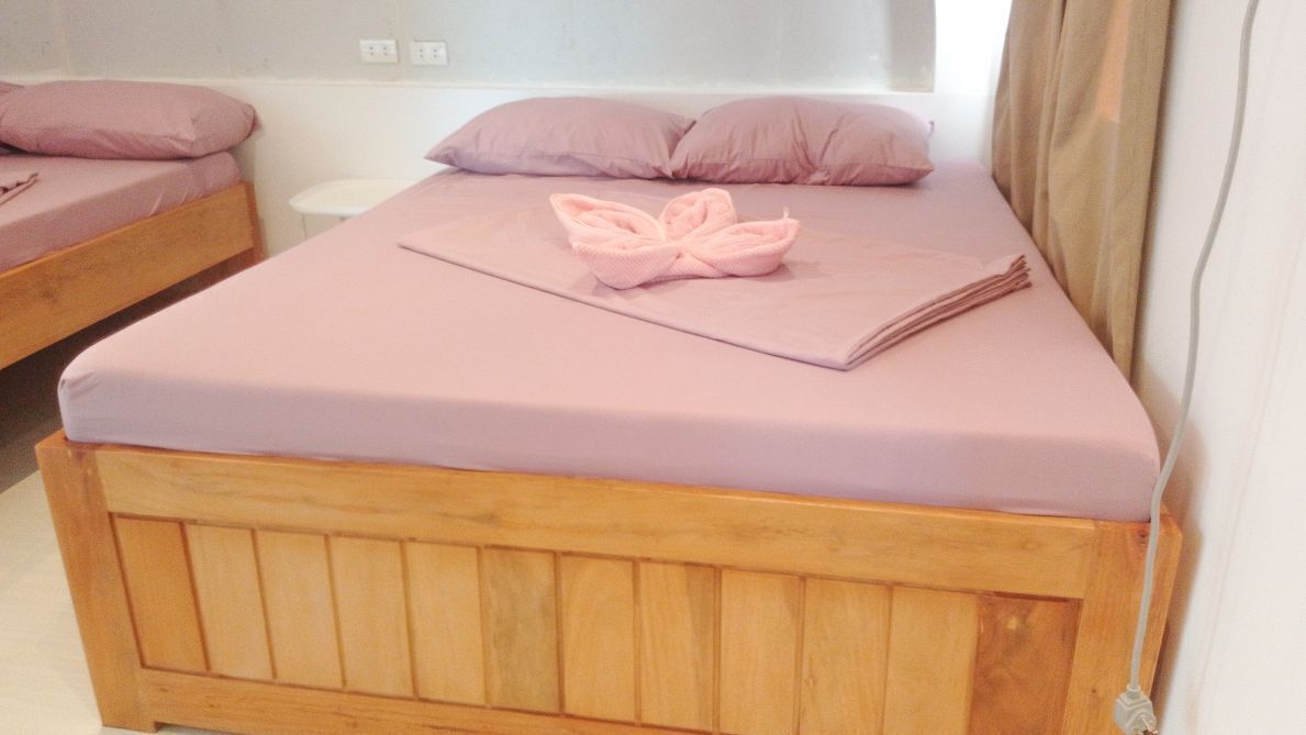 Un lit simple avec une tête de lit en bois, une couvre-lit rose et une serviette rose pliée au centre.