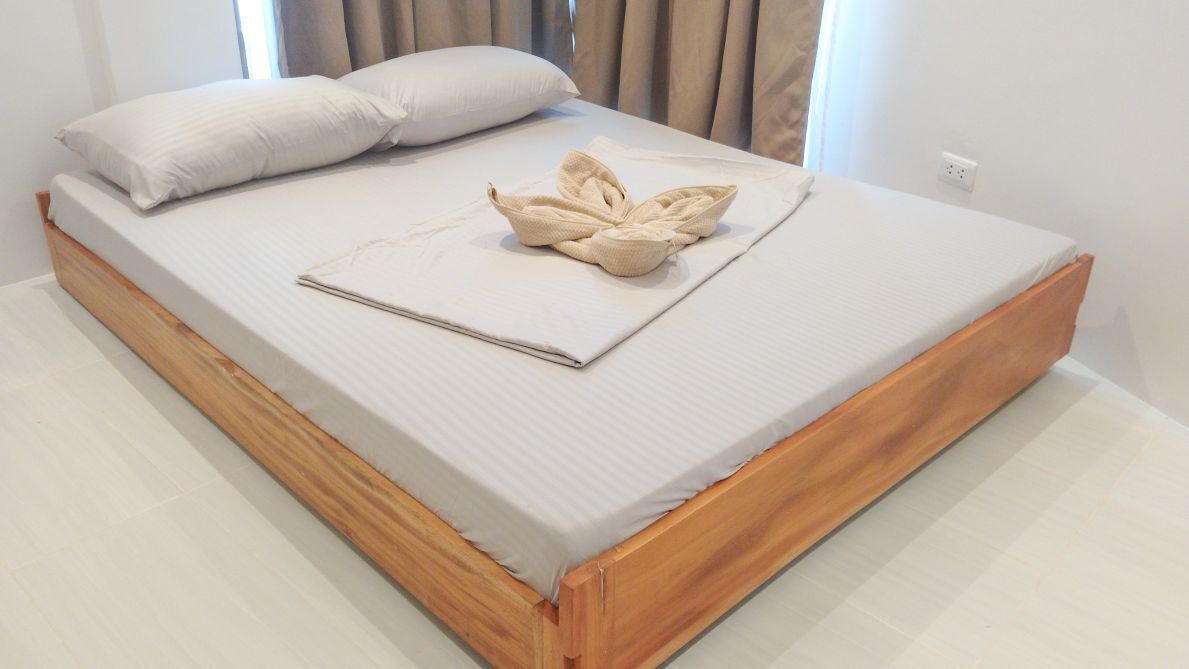 Una cama bien hecha con cabecera de madera, una colcha doblada y dos almohadas.
