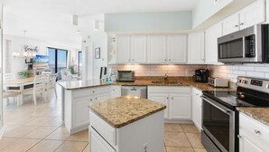 A modern kitchen with white cabinets, granite countertops, a built-in microwave, and a large island. - Bluewater 1501 | Beach Front (Orange Beach)