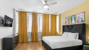 A bedroom with a bed, a ceiling fan, a TV, and a window with curtains.