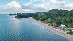 A coastal landscape with a beach, a small island, and a mountain range in the background.
