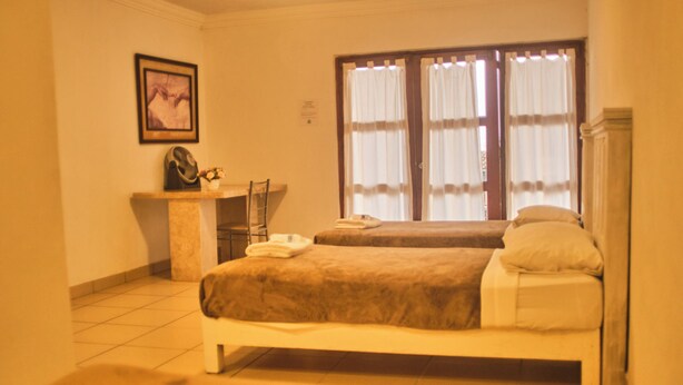 A hotel room with two beds, a desk, a chair, and a window with curtains. - Jardin Zen  (Tepoztlán)