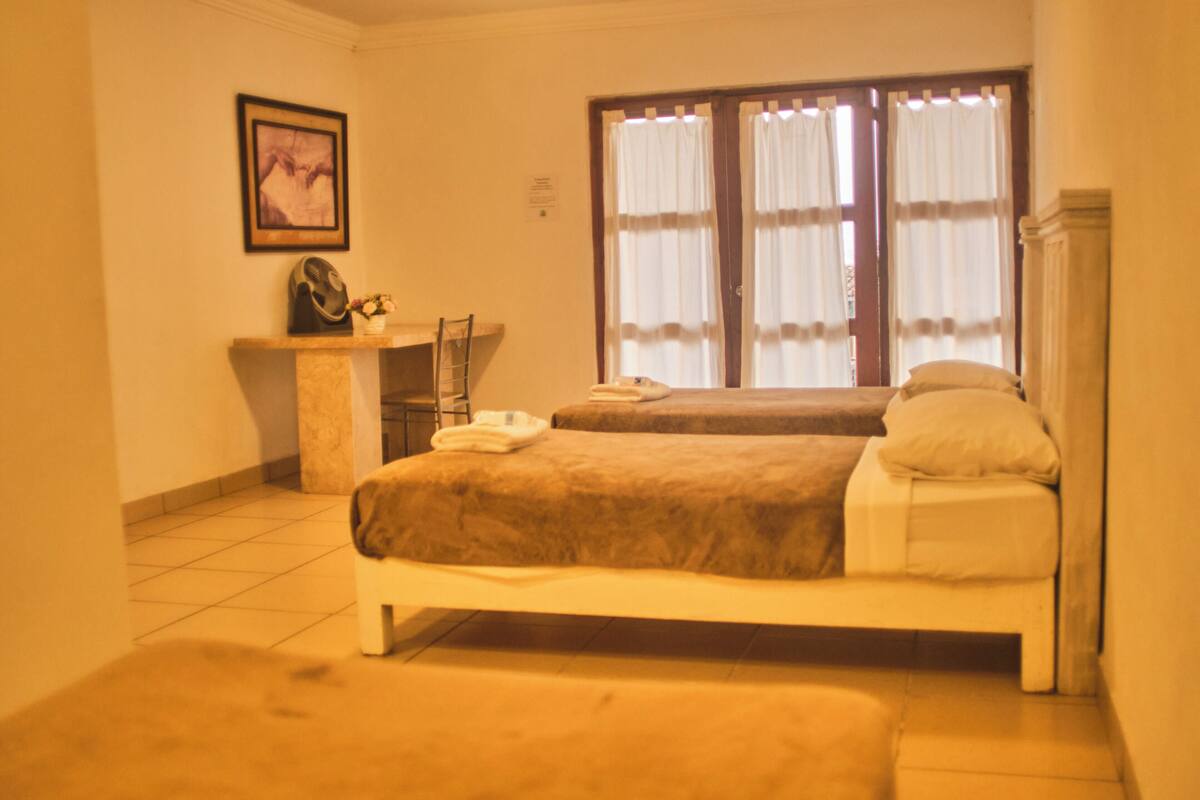A hotel room with two beds, a desk, a chair, and a window with curtains.