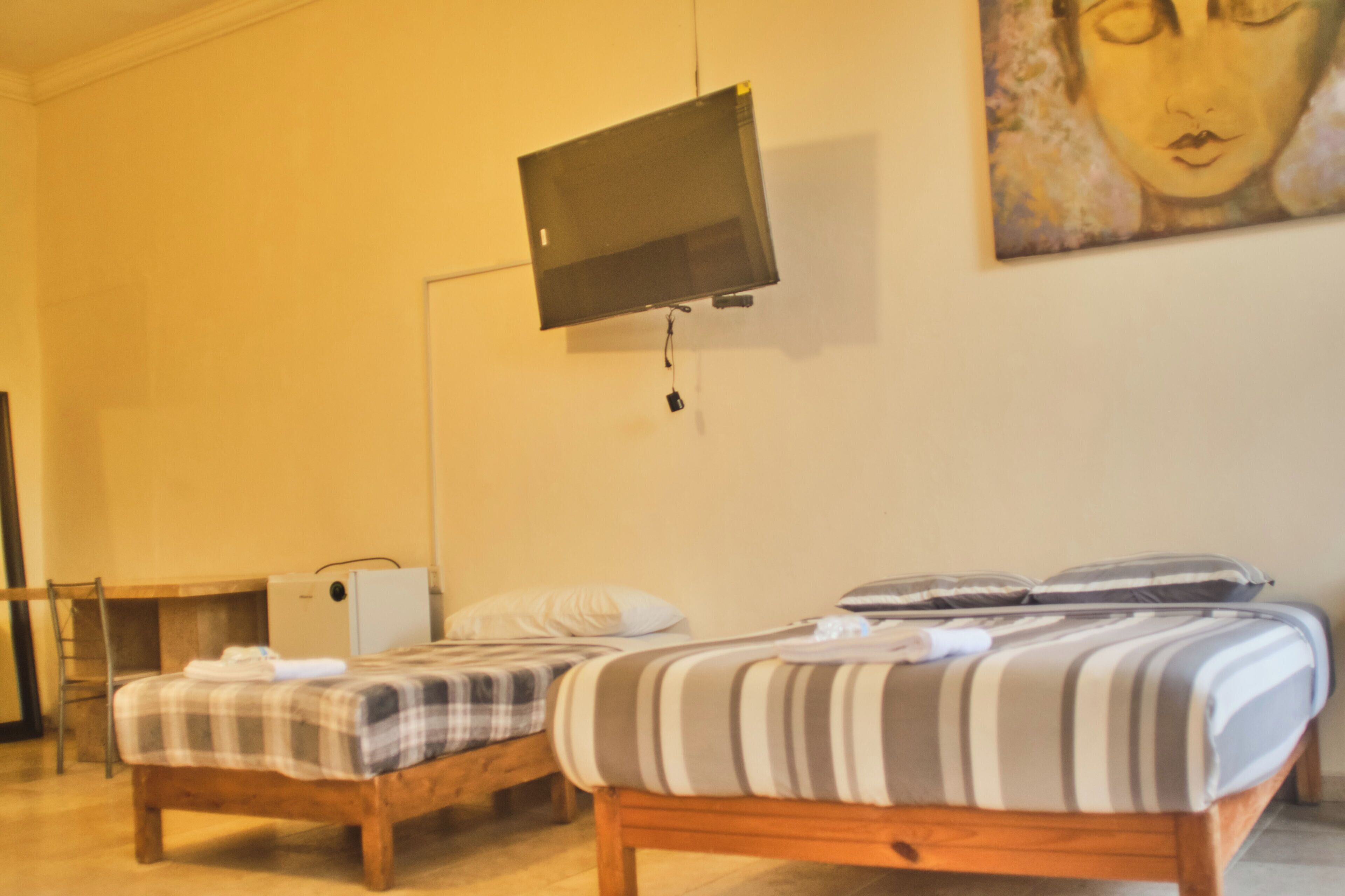 A room with two wooden beds, a television mounted on the wall, and a painting.