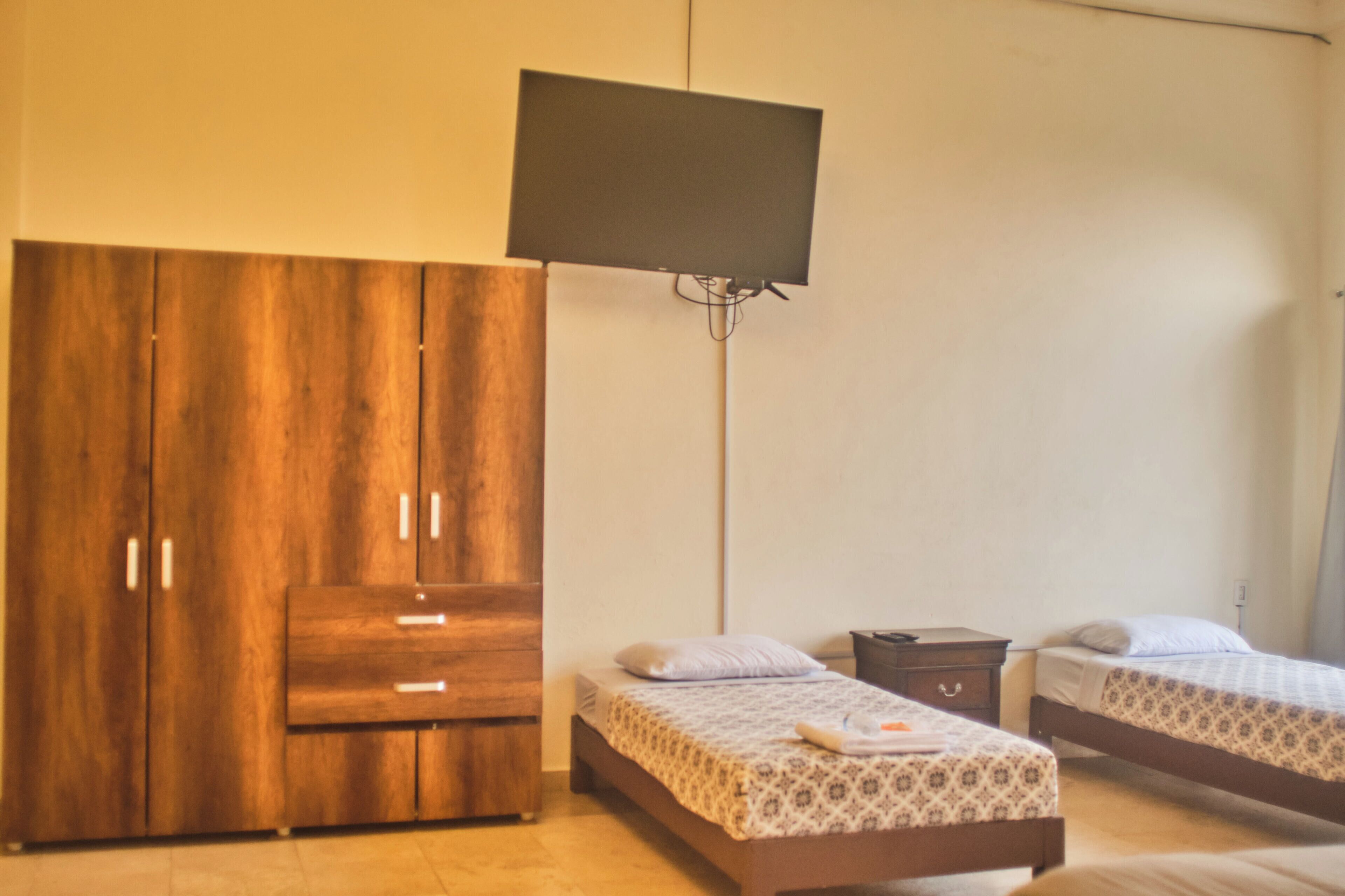 Ein Schlafzimmer mit zwei Betten, einem Kleiderschrank und einem an der Wand befestigten Fernseher.