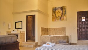A hotel room with a bed, a bathroom with a bathtub, a painting on the wall, and a door. - Jardin Zen  (Tepoztlán)