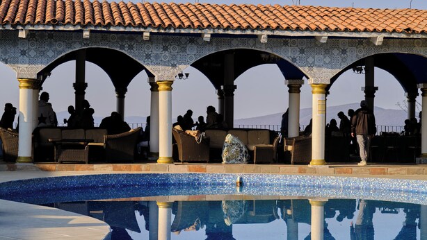 A pool area with tiled flooring, a tiled roof, and a seating area with chairs and tables.