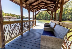 A wooden deck with wicker furniture overlooking a lake. - SEBOU, a cozy stay for four in the lodge of Karoo at Smith Mountain Lake (Wirtz)