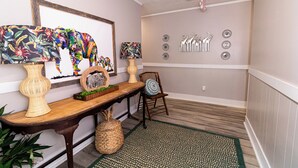 Un couloir avec une table en bois, deux vases, une chaise et des œuvres d’art décoratives accrochées au mur.