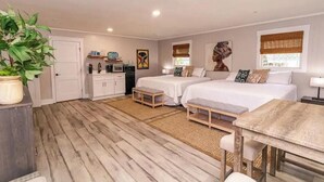 A bedroom with two beds, a wooden dining table, a kitchen area, and a large potted plant. - CARACUL, a cozy stay for four in the lodge of Karoo at Smith Mountain Lake  (Wirtz)