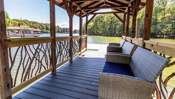 A wooden deck with wicker furniture overlooking a lake. - CARACUL, a cozy stay for four in the lodge of Karoo at Smith Mountain Lake  (Wirtz)