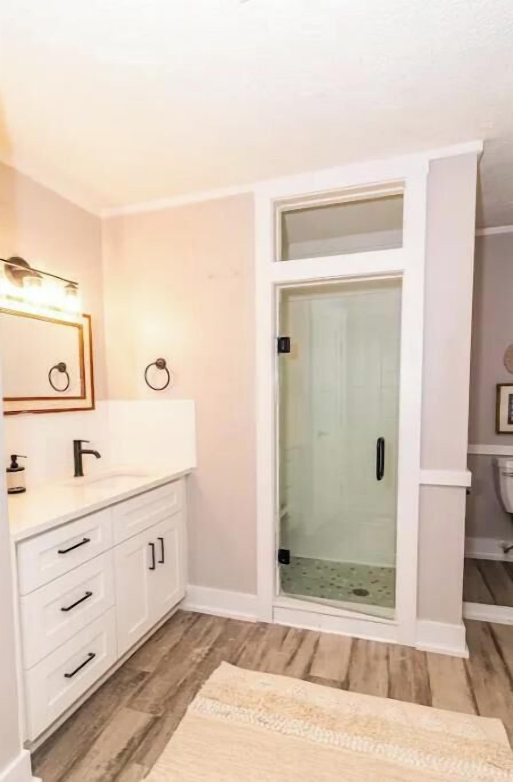 A bathroom with a white vanity, a glass shower enclosure, and a wooden floor.