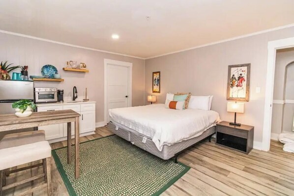 A bedroom with a bed, bedside tables, a desk, and a kitchenette.