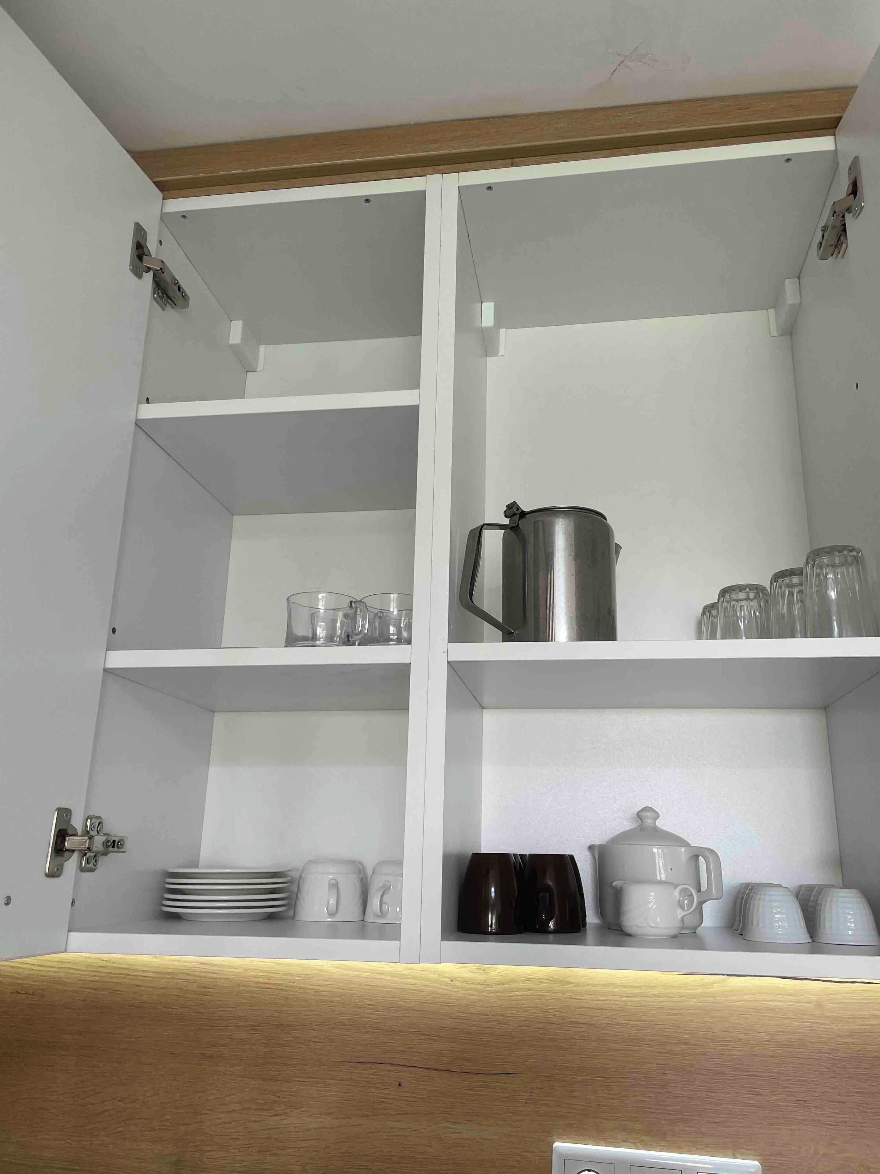 Une cuisine avec des meubles blancs, un plan de travail en bois et divers ustensiles de cuisine, notamment des assiettes, des tasses et une bouilloire.